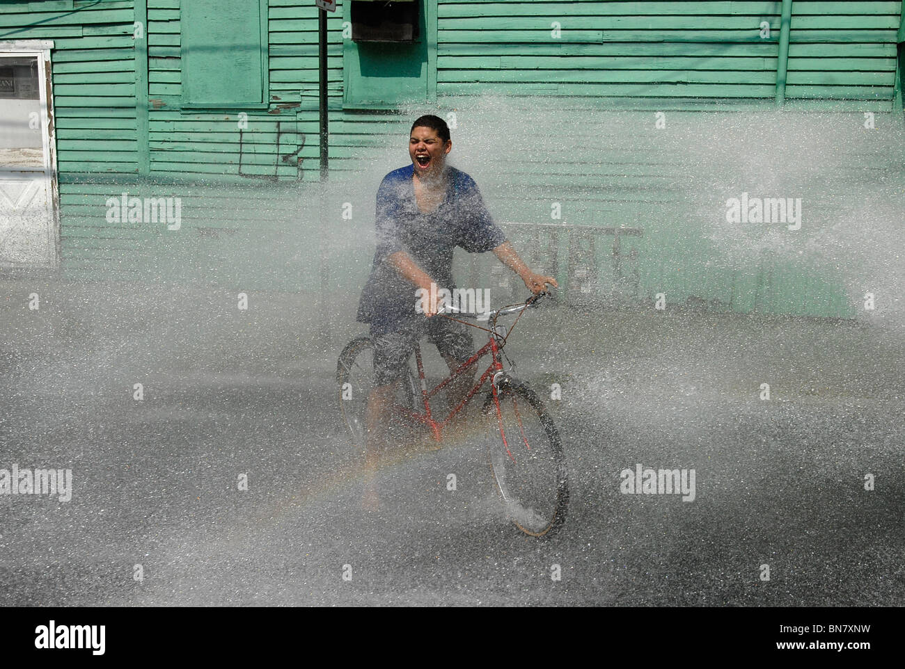 Eine junge Teen reitet durch das Spray von einer offenen Hydranten während einer Hitzewelle in New Haven CT USA wo Temps über 100 F waren. Stockfoto