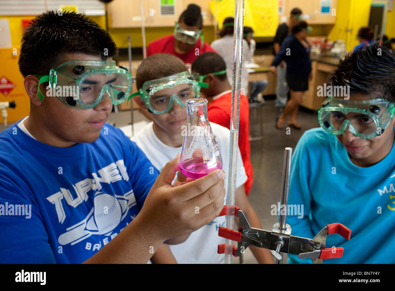Hispanische High-School-jungen in Schutzbrille betrachten Lösung in Kolben während der Titration Experiment im Chemieunterricht Stockfoto