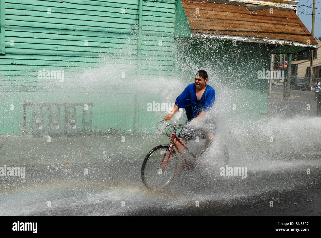 Eine junge Teen reitet durch das Spray von einer offenen Hydranten während einer Hitzewelle in New Haven CT USA wo Temps über 100 F waren. Stockfoto