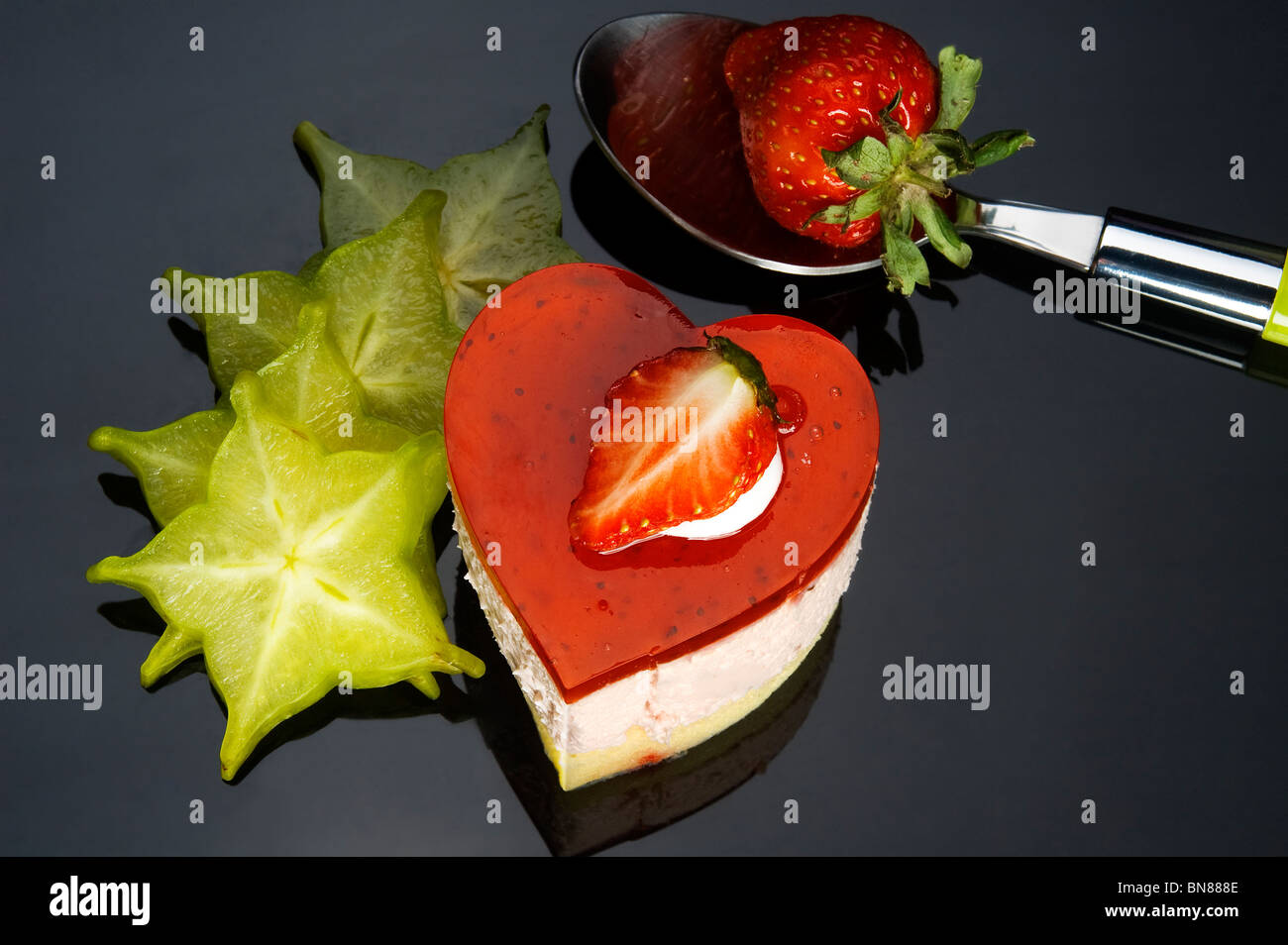 herzförmige Erdbeerkuchen mit Karambolen oder Sternfrucht Dekor auf schwarzem Hintergrund Stockfoto