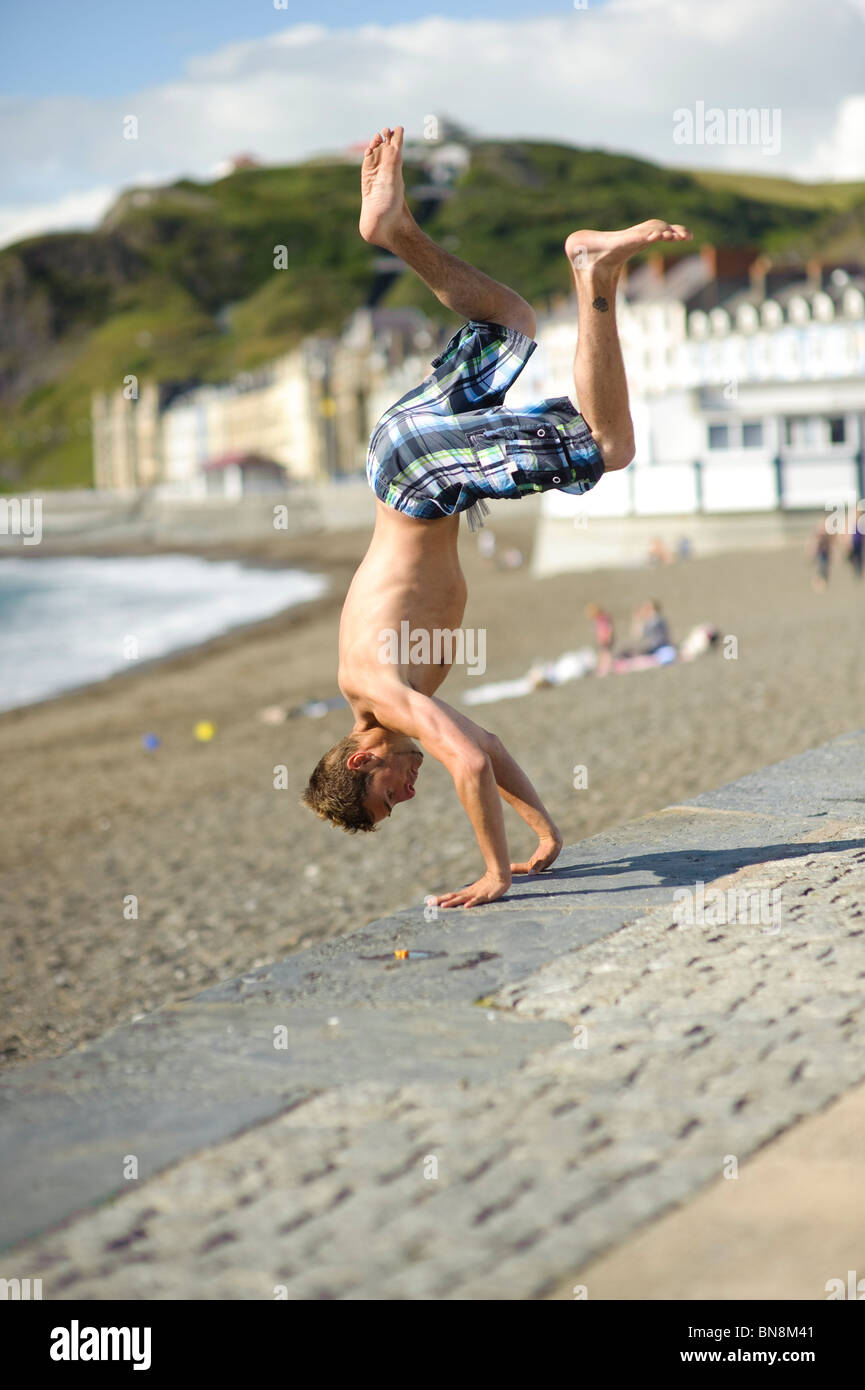 Ein Teenager junge Mann tut Parkour Freerunning Stunt auf Aberystwyth Promenade an einem Sommernachmittag, Wales UK Stockfoto