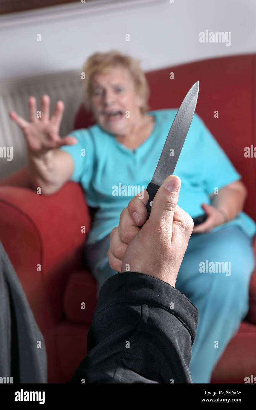 Messer gezogen als verängstigte ältere Frau sieht in Richtung der Angreifer Stockfoto