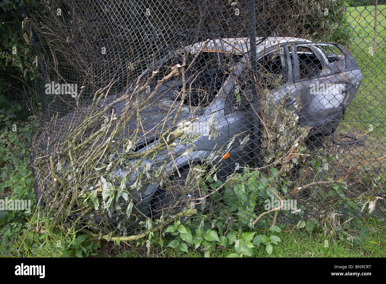 gestohlenes Auto prallte gegen einen Maschendrahtzaun in Großbritannien ausgebrannt Stockfoto