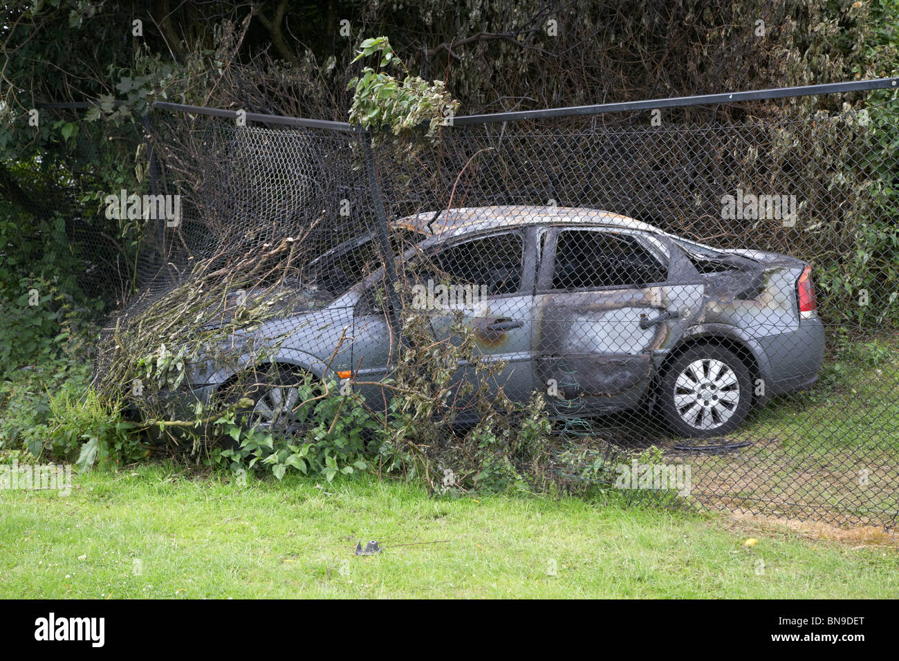 gestohlenes Auto prallte gegen einen Maschendrahtzaun in Großbritannien ausgebrannt Stockfoto