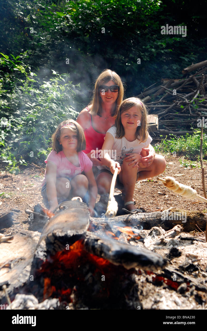 Mutter mit ihren 2 Töchtern (im Alter von 5 & 7) "Dämpfer" Backen (Teig gebacken auf offenem Feuer machen Brot) an einem Pfadfinder-Feier-Tag. Stockfoto