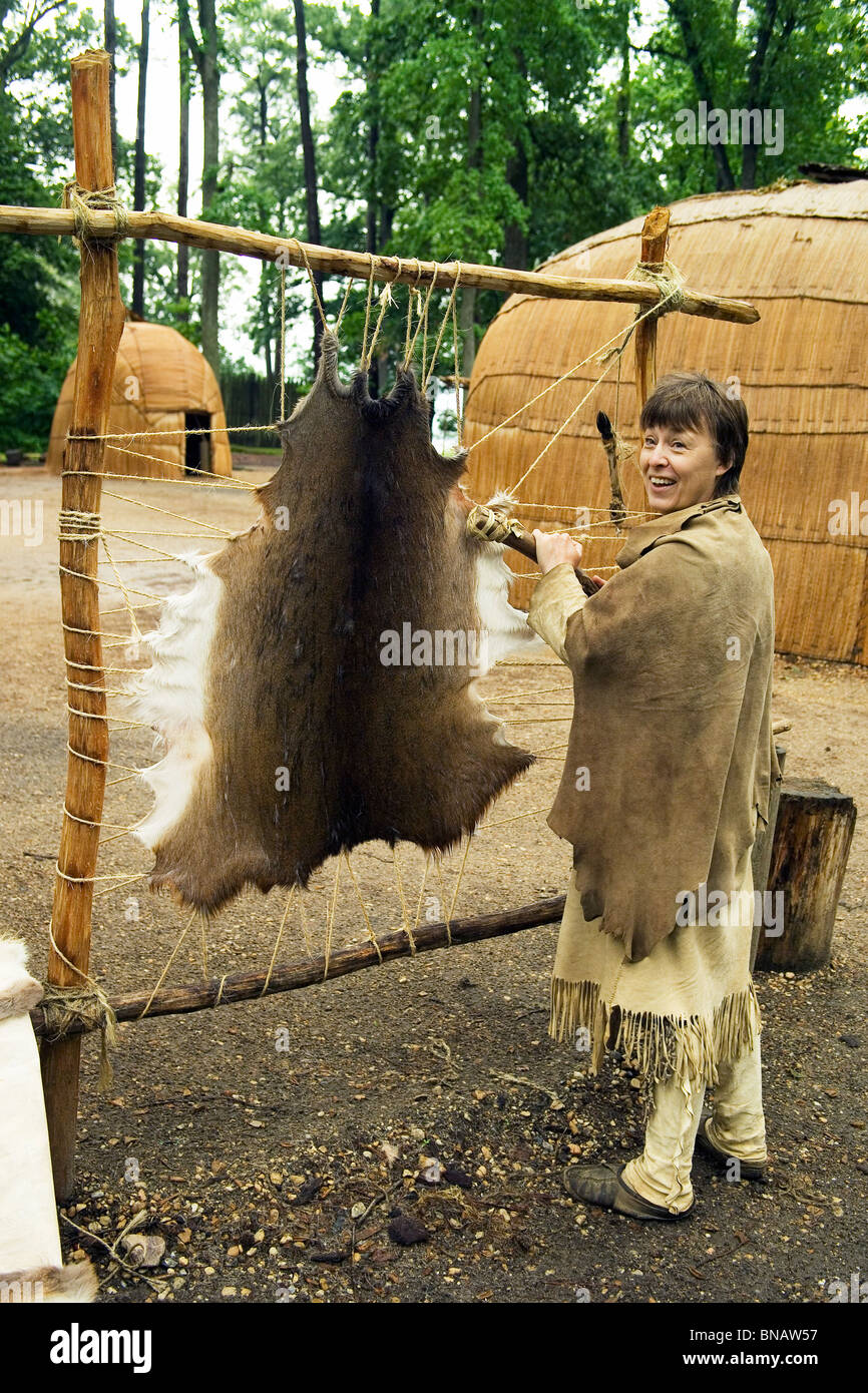Dolmetscher, gekleidet wie ein Powhatan-Indianer schabt eine Tierhaut um Besucher in das frühe 1600 s in Jamestown Regelung, Virginia, USA Leben zeigen. Stockfoto