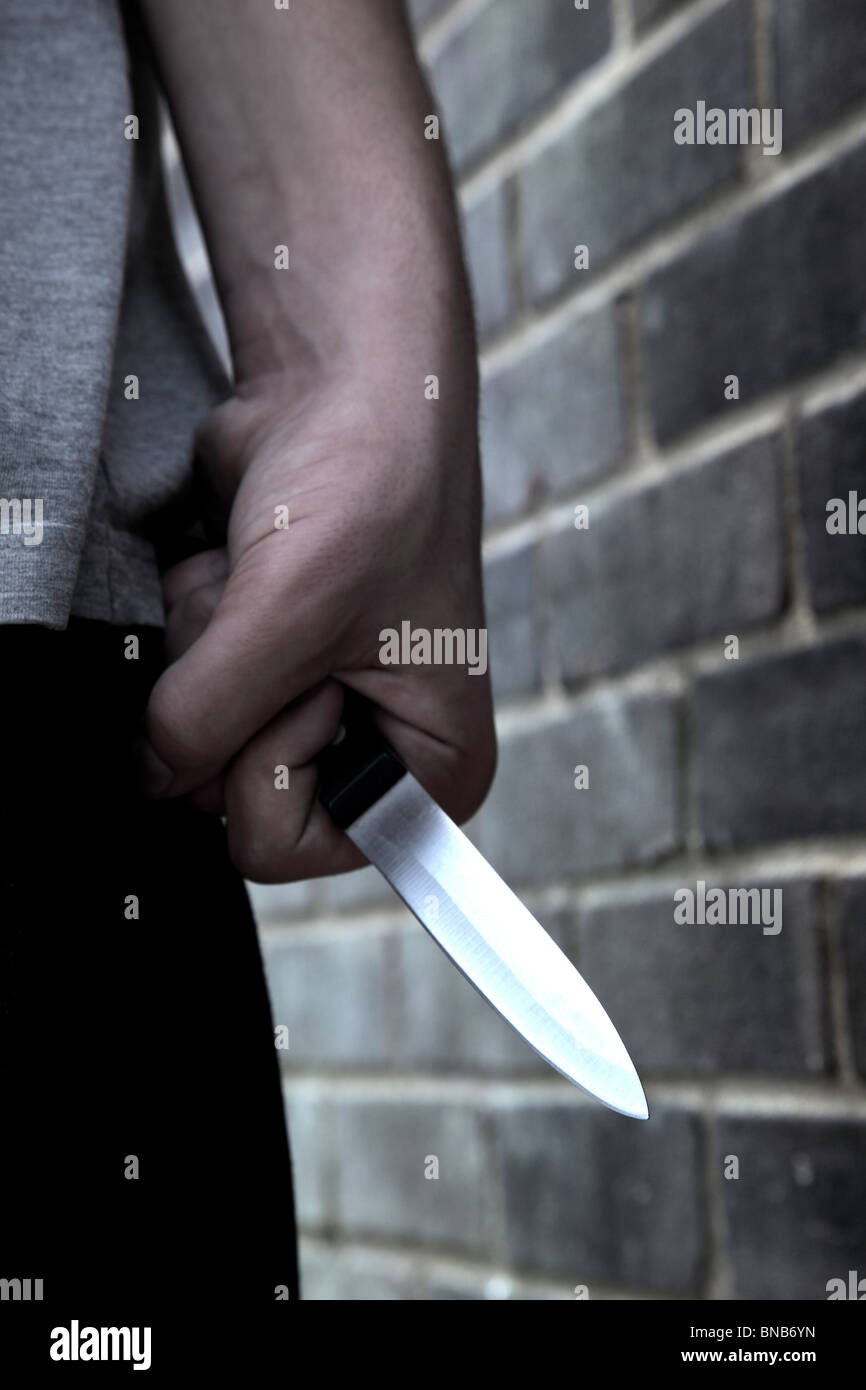Hand von einem jungen Mann mit einem Messer, vorbei an einer Mauer Stockfoto