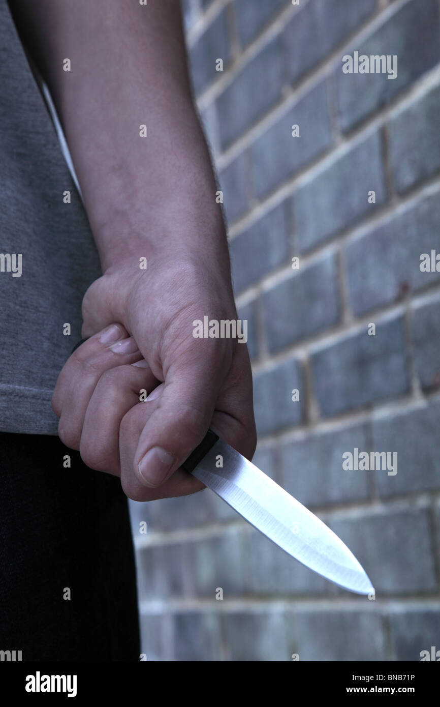 Hand von einem jungen Mann mit einem Messer, vorbei an einer Mauer Stockfoto