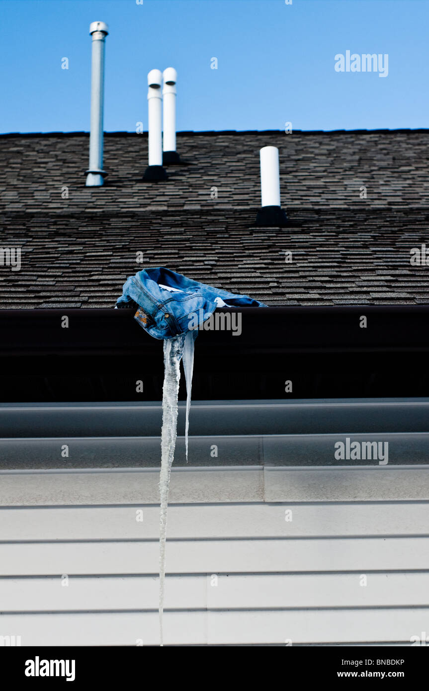 Ein großer Eiszapfen hängt prekär aus einem verlassenen paar Hosen auf einem Dach Stockfoto