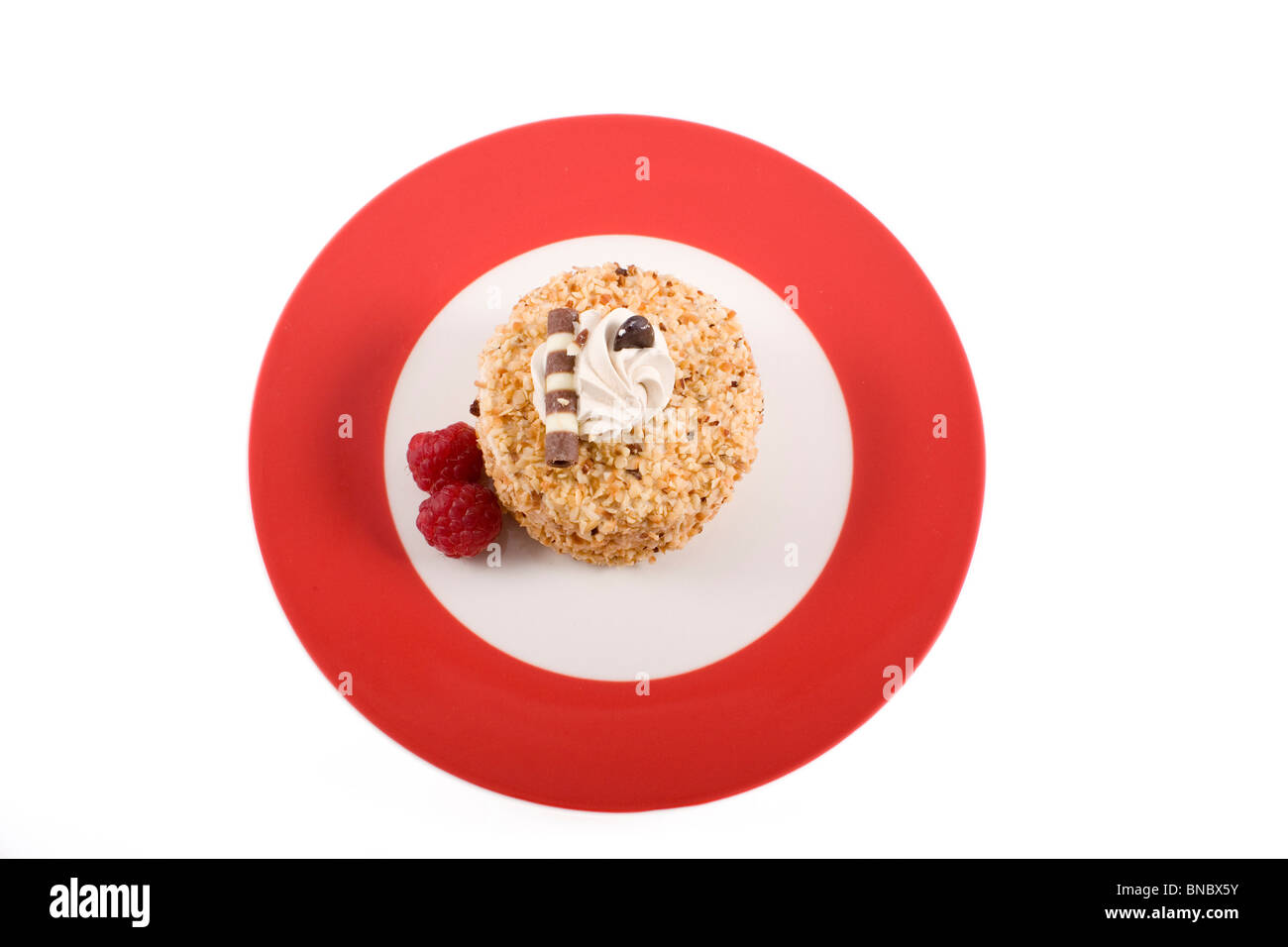 Haselnusskuchen auf rotem Teller mit Himbeeren. Schoss aus direkt oben und isoliert auf weißem Hintergrund. Stockfoto