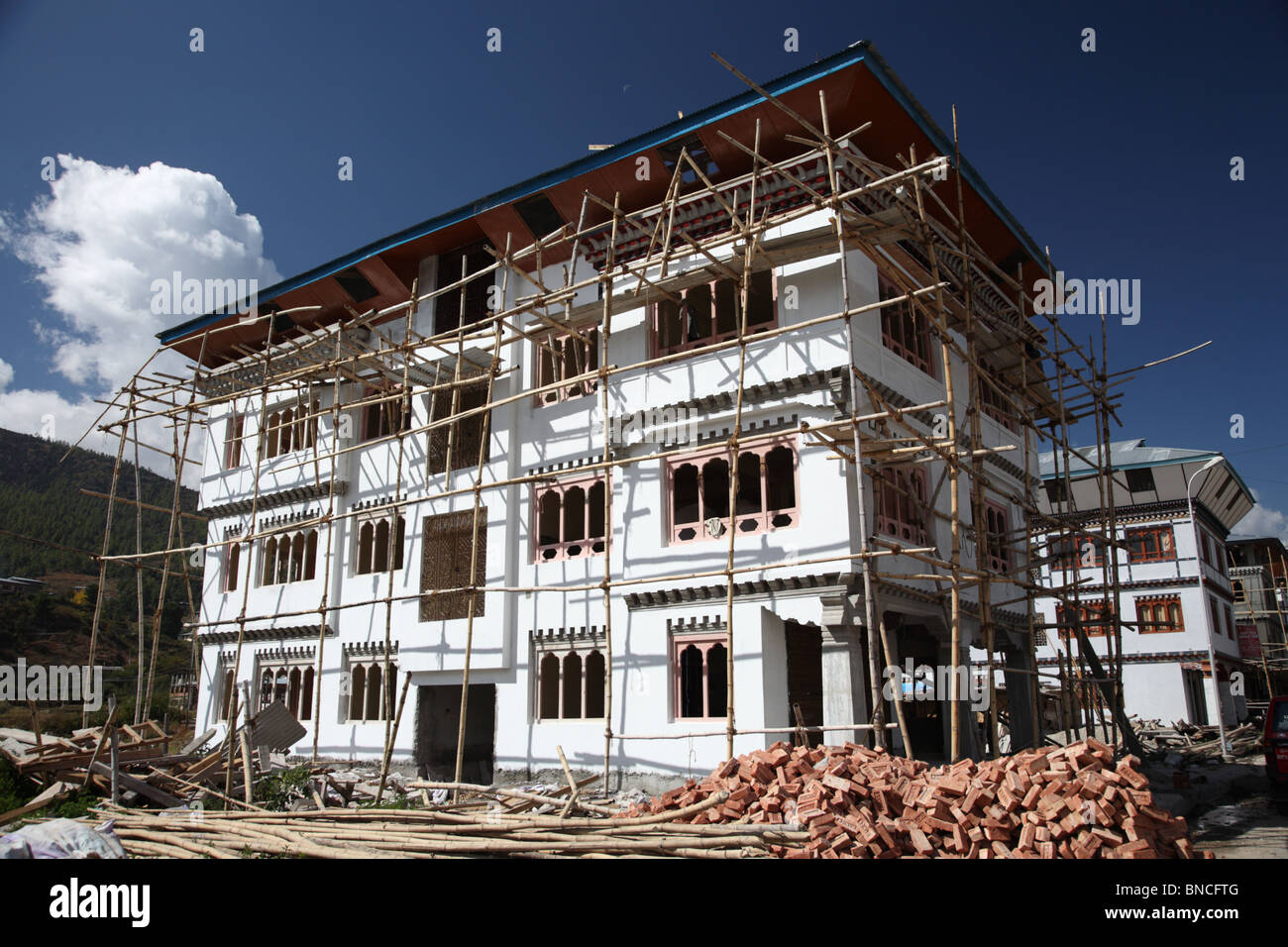 Ein großes Haus im Bau, umgeben von Bambus-Gerüst und Haufen von Steinen in Paro, Bhutan. Stockfoto