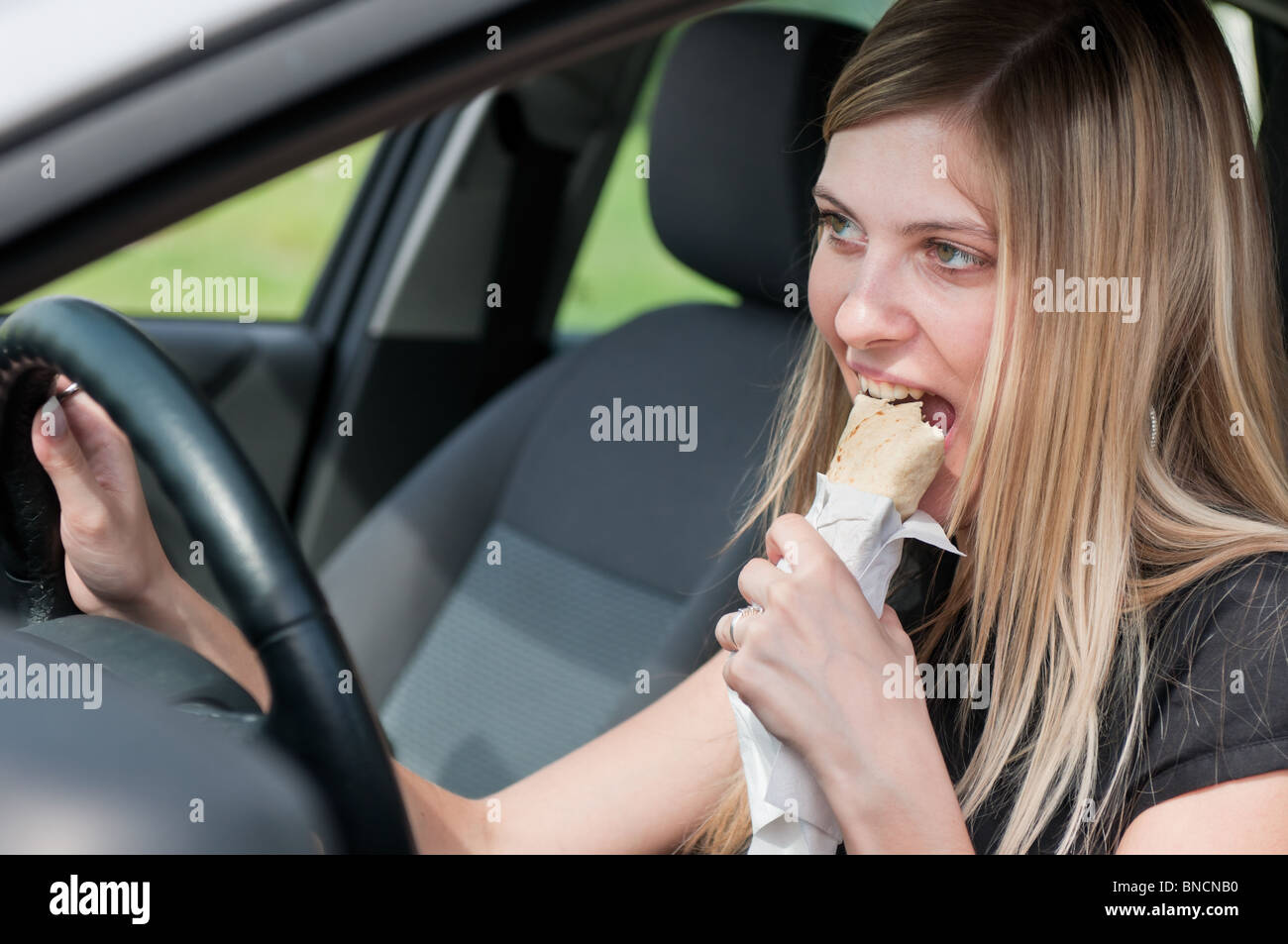 Junge schöne lächelnde Frau Auto und Essen Fast-Food - Porträt durch Seitenfenster Stockfoto
