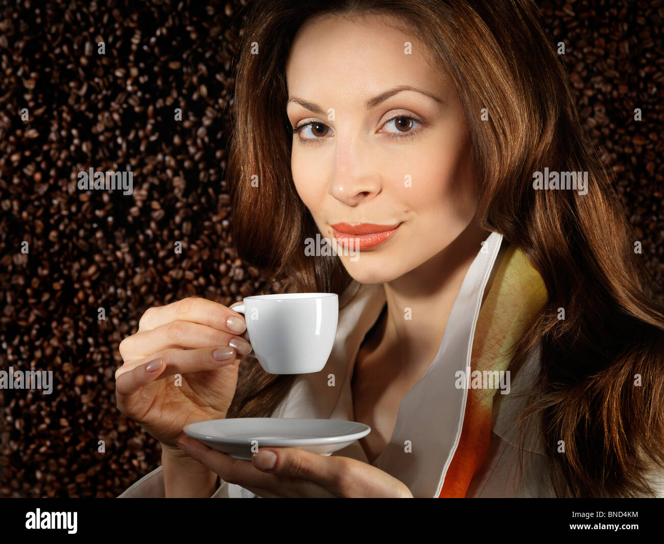 Schöne junge Frau hält eine Tasse Kaffee mit Kaffeebohnen Hintergrund hinter ihr Stockfoto