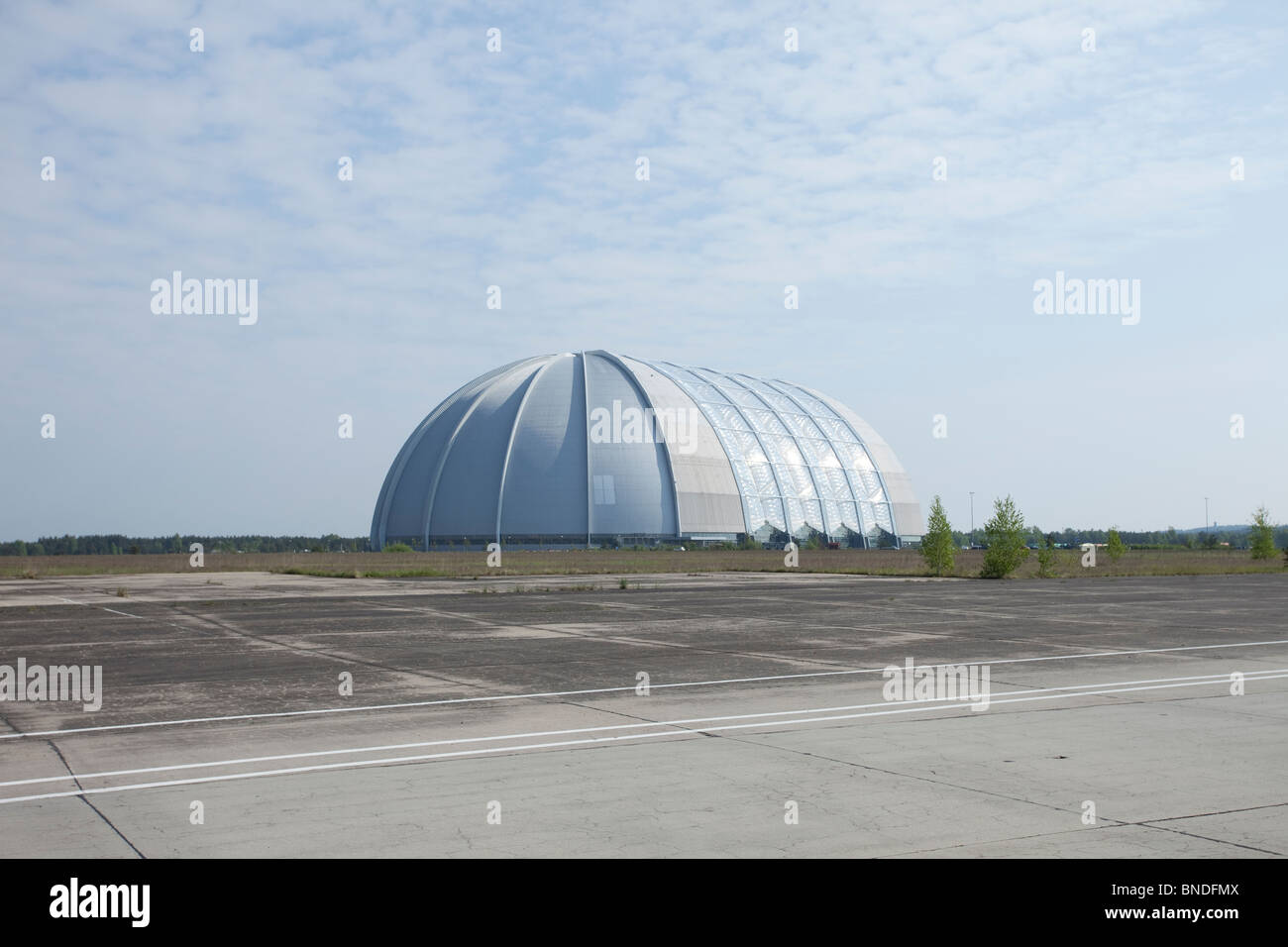 Weitläufiger Blick auf den ehemaligen Zeppelin-Luftschiff-Hangar, heute eine massive Kuppelstruktur unter blauem Himmel, an einem verlassenen Flugplatz in Deutschland. Stockfoto