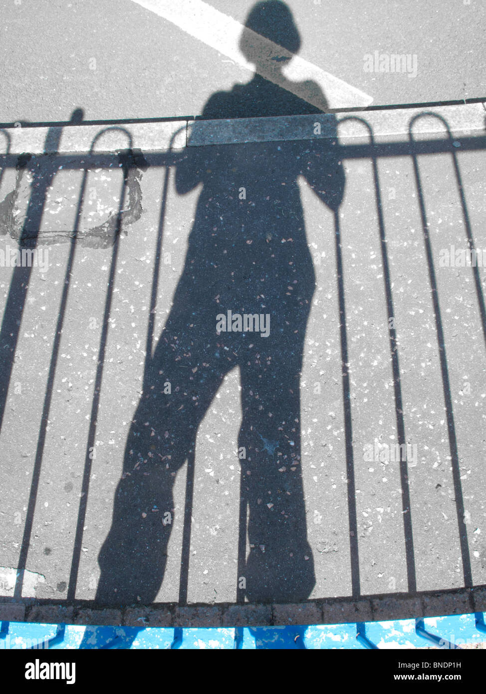 Schatten einer Person und Geländer auf eine asphaltierte Straße. Stockfoto