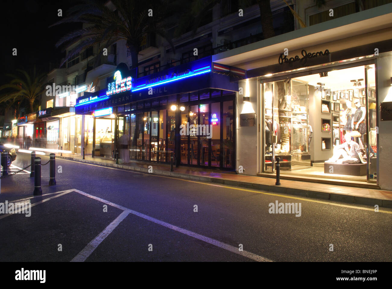Geschäfte und Restaurants entlang der Uferpromenade in der Nacht, Puerto Banus, Marbella, Costa Del Sol, Provinz Malaga, Andalusien, Spanien. Stockfoto
