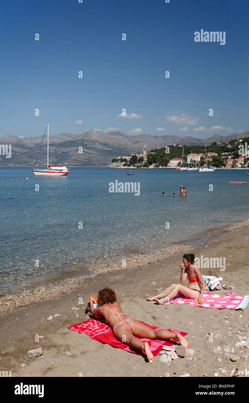Frauen, Sonnenbaden am Strand und Blick auf Hafen Lopud Süd Dalmatien Kroatien dalmatinische kroatischen Insel Elafiti Elaphiten Inseln Stockfoto