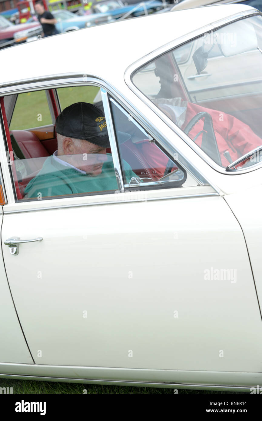 Paar Rentner Einschlafen am Steuer ihrer weißen Oldtimer bei einer Kundgebung im Sommer tragen Kappen und Brillen Stockfoto