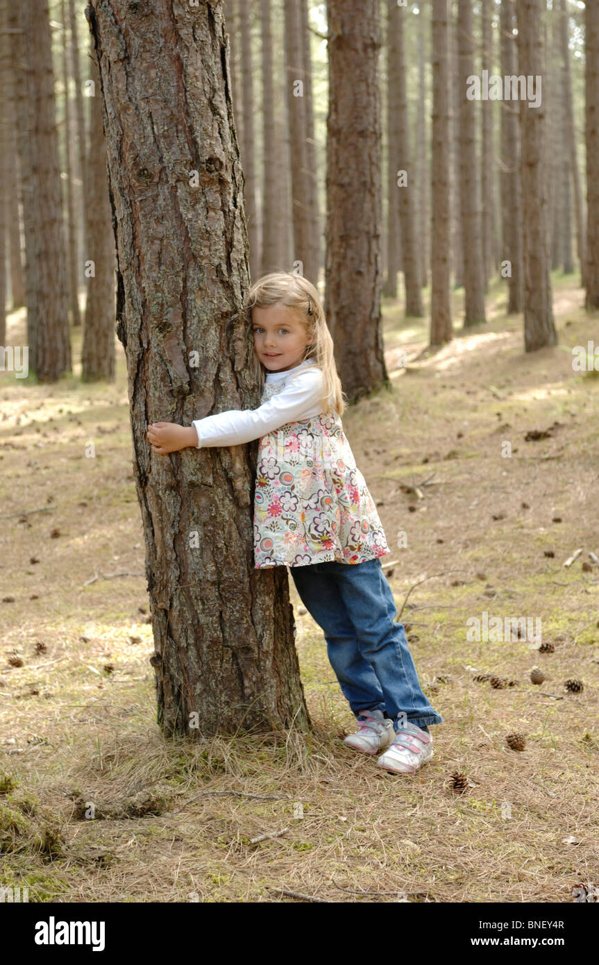 Eine 5-jährige Kindergartenalter weiße Mädchen umarmt einen Baumstamm in Roseisle Moray Schottland. Stockfoto