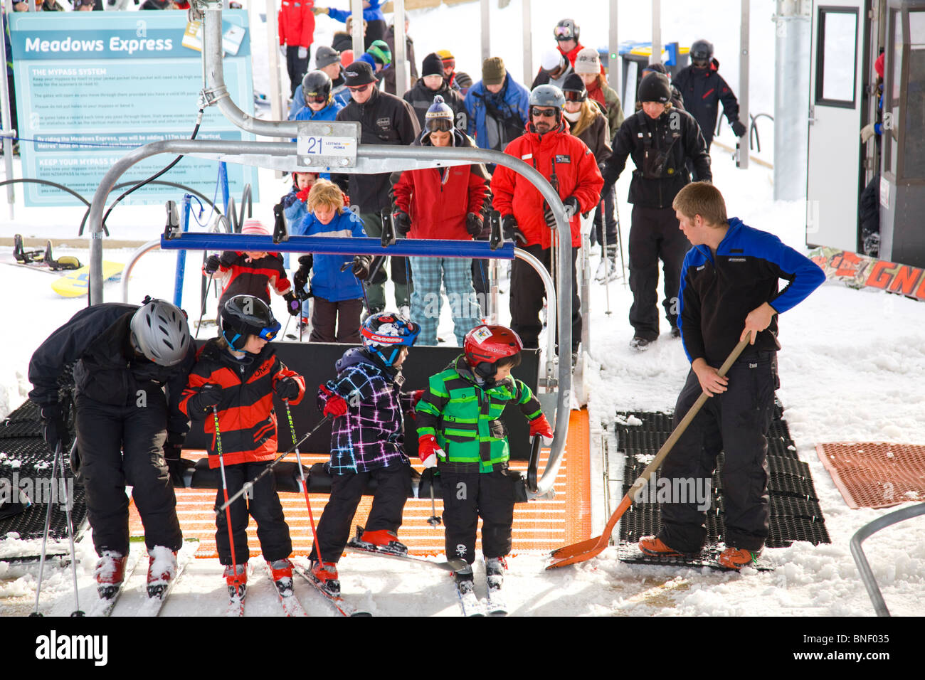 Drei Kinder und ein Erwachsener steigen auf den Meadows Express Sessellift im Coronet Peak Ski Resort, Queenstown, Neuseeland Stockfoto