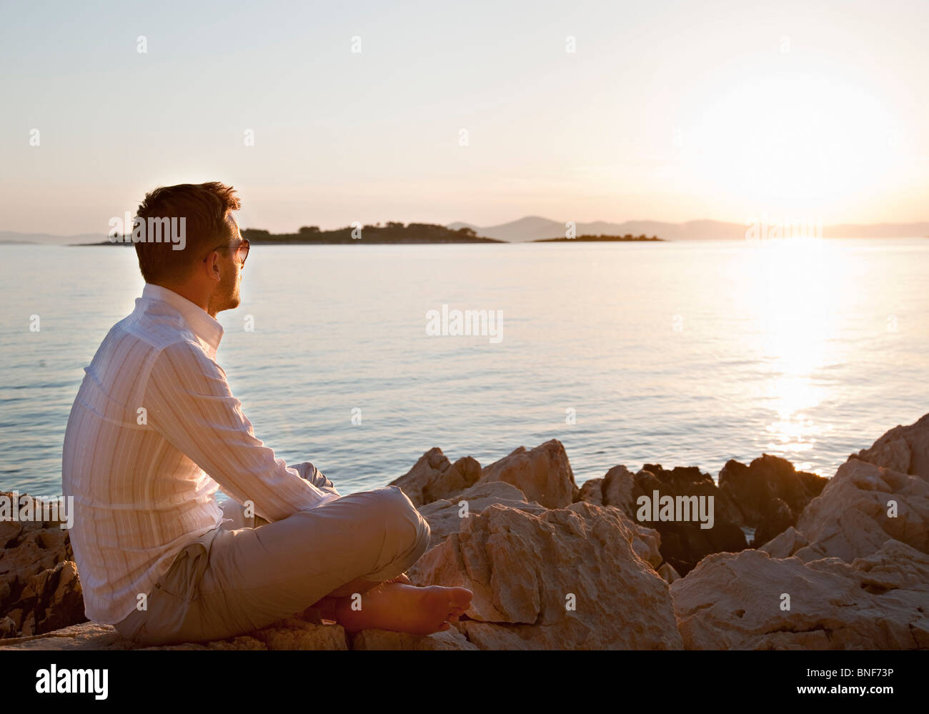 Mann beobachten Sonnenuntergang am felsigen Strand Stockfoto