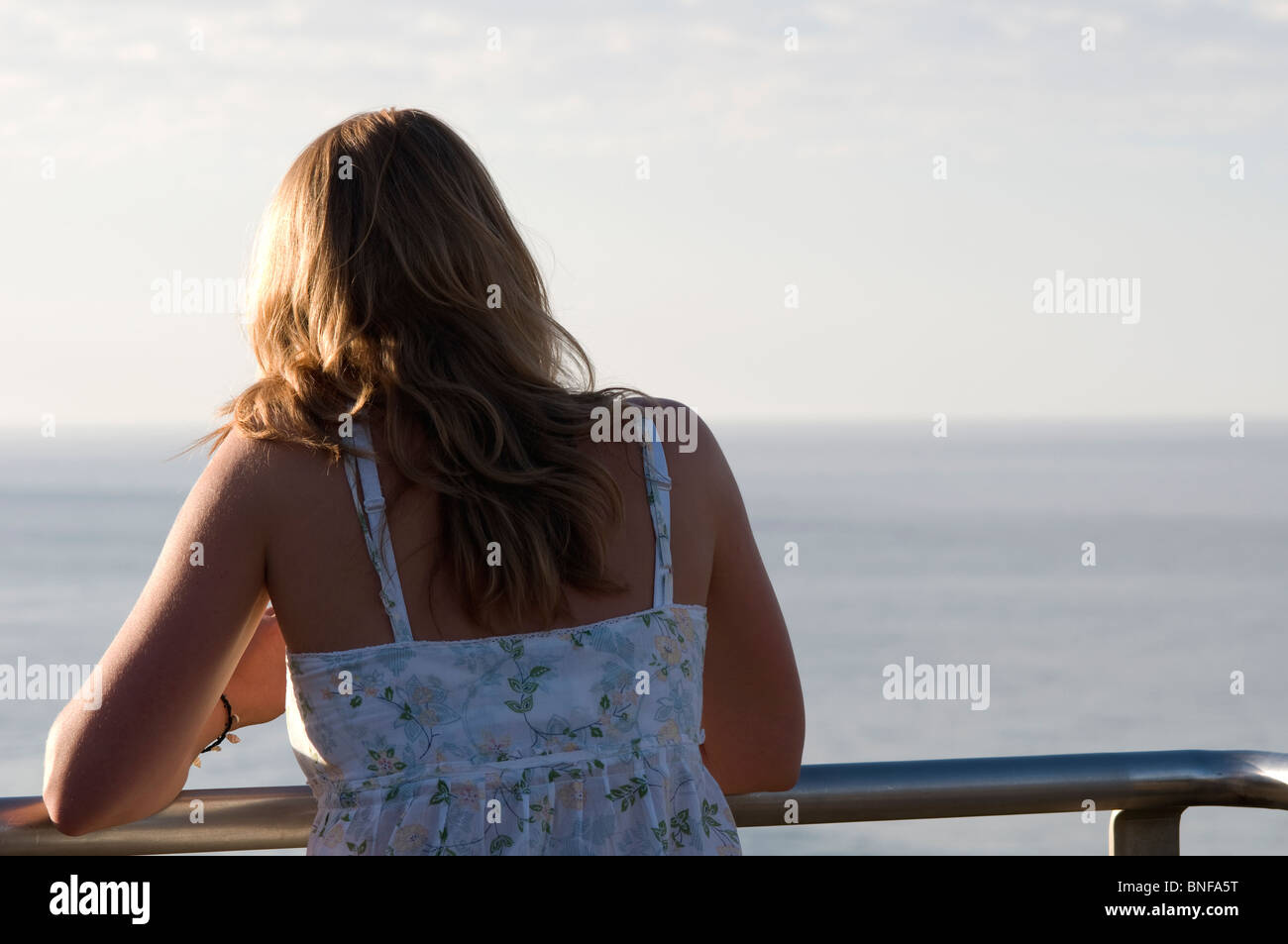 Rückansicht der Frau steht auf einem Balkon mit Blick auf den Ozean Stockfoto