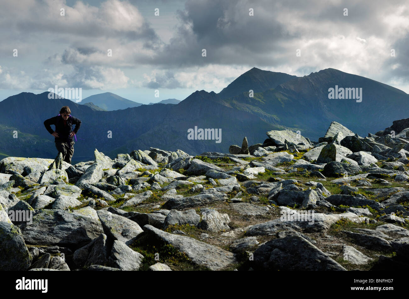 Mittleren Alters Wanderer erreichen die Spitze den Glyder Fach/Fawr Grat mit den Gipfeln des Mount Snowdon Bereichs im Hintergrund. Stockfoto