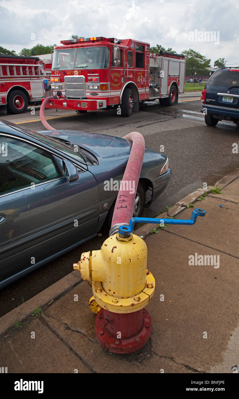 Detroit, Michigan - ein Feuerwehrschlauch wird über ein falsch geparktes Auto auf einen Hydranten drapiert, wie Feuerwehrleute einen Hausbrand kämpfen. Stockfoto