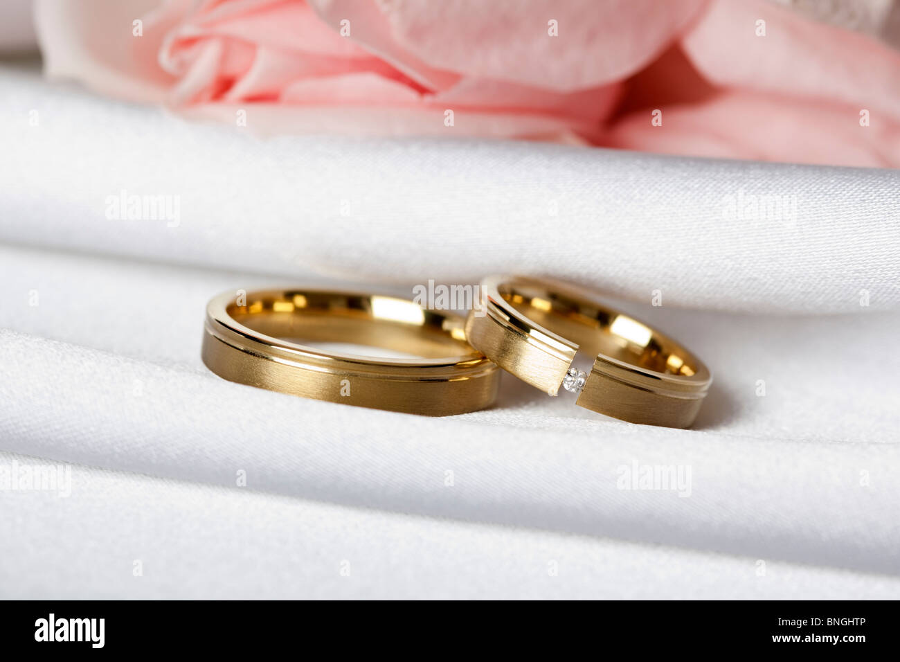 Goldene Hochzeit Ringe auf Seide, rosa Rosen im Hintergrund Stockfoto