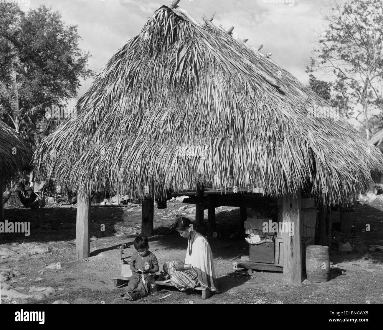 USA, Florida, Seminole Frau sitzt mit Sohn (4-5) bei strohgedeckten Hütte Stockfoto