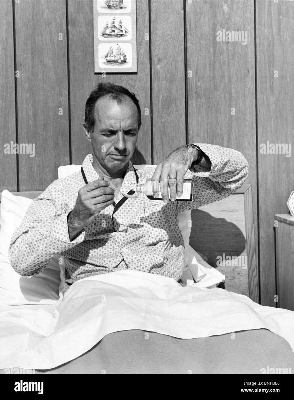 Reifer Mann im Bett Gießen Medizin in einem Löffel Stockfoto
