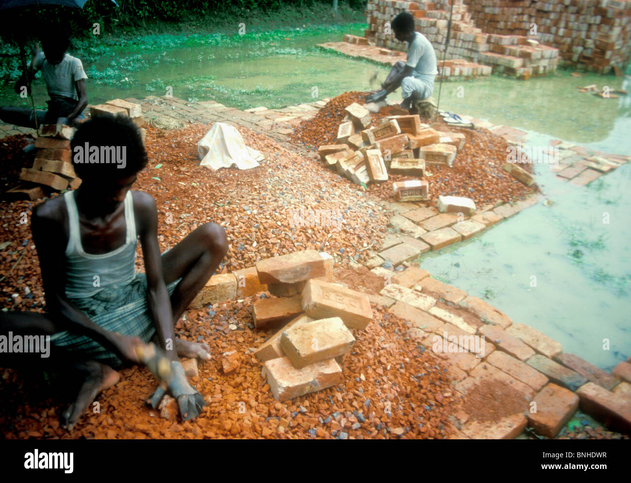 Arme Männer Ziegel zerkleinern, Zuschlagstoff für Strassenbau Bangladesch machen Stockfoto