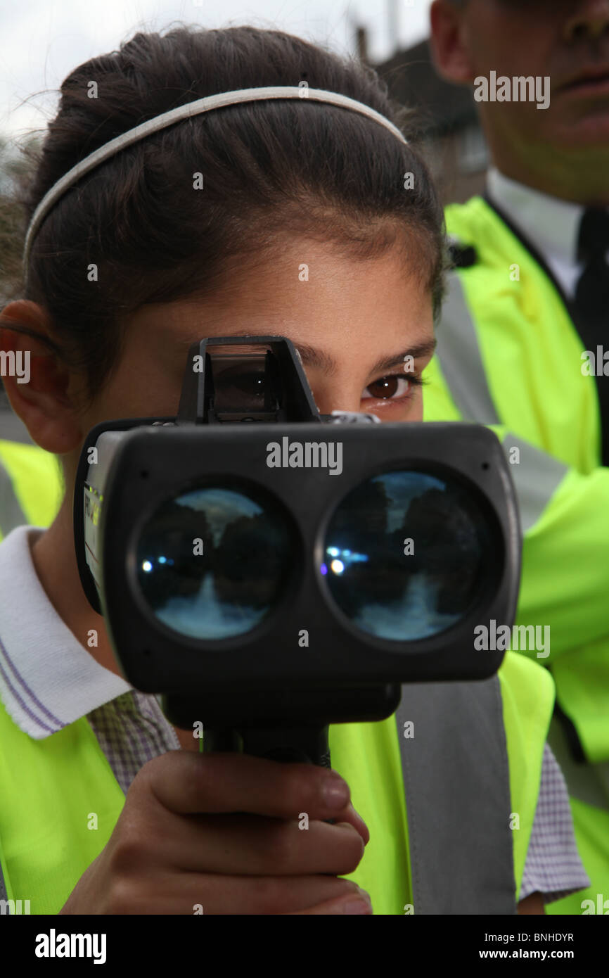 ein Schulmädchen mit einer Geschwindigkeit-Pistole mit einem Polizisten stoppen Beschleunigung Autofahrer außerhalb ihrer Schule Stockfoto