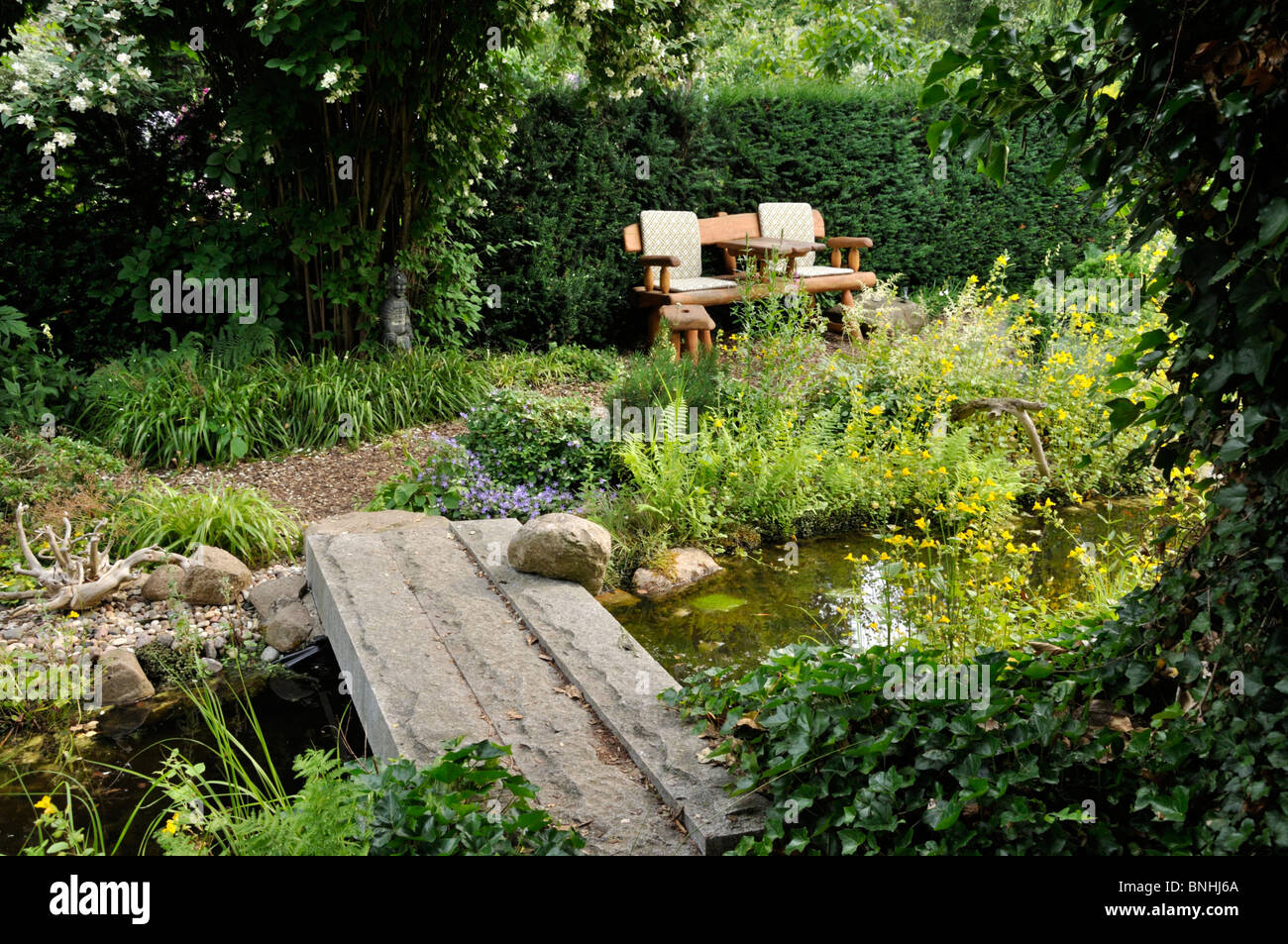Garten Bank an einem Teich mit Brücke aus Stein. Design: Marianne und Detlef lüdke Stockfoto