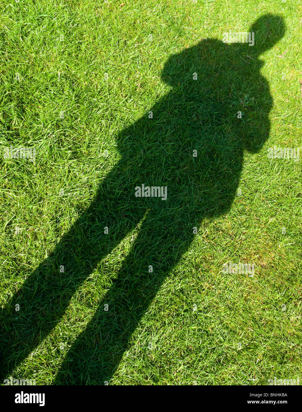 Diagonale Schatten der männlichen Figur stehend auf dem grünen Rasen Stockfoto