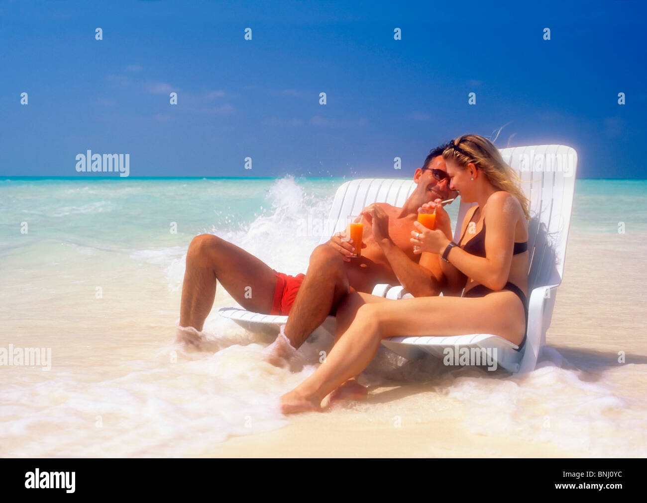 Paar paar 20 30 Urlaub Ferien Reisen Malediven Strand Küste Liegestuhl Bikini trinken Wasser Mann Mann Frau Meereswellen Stockfoto