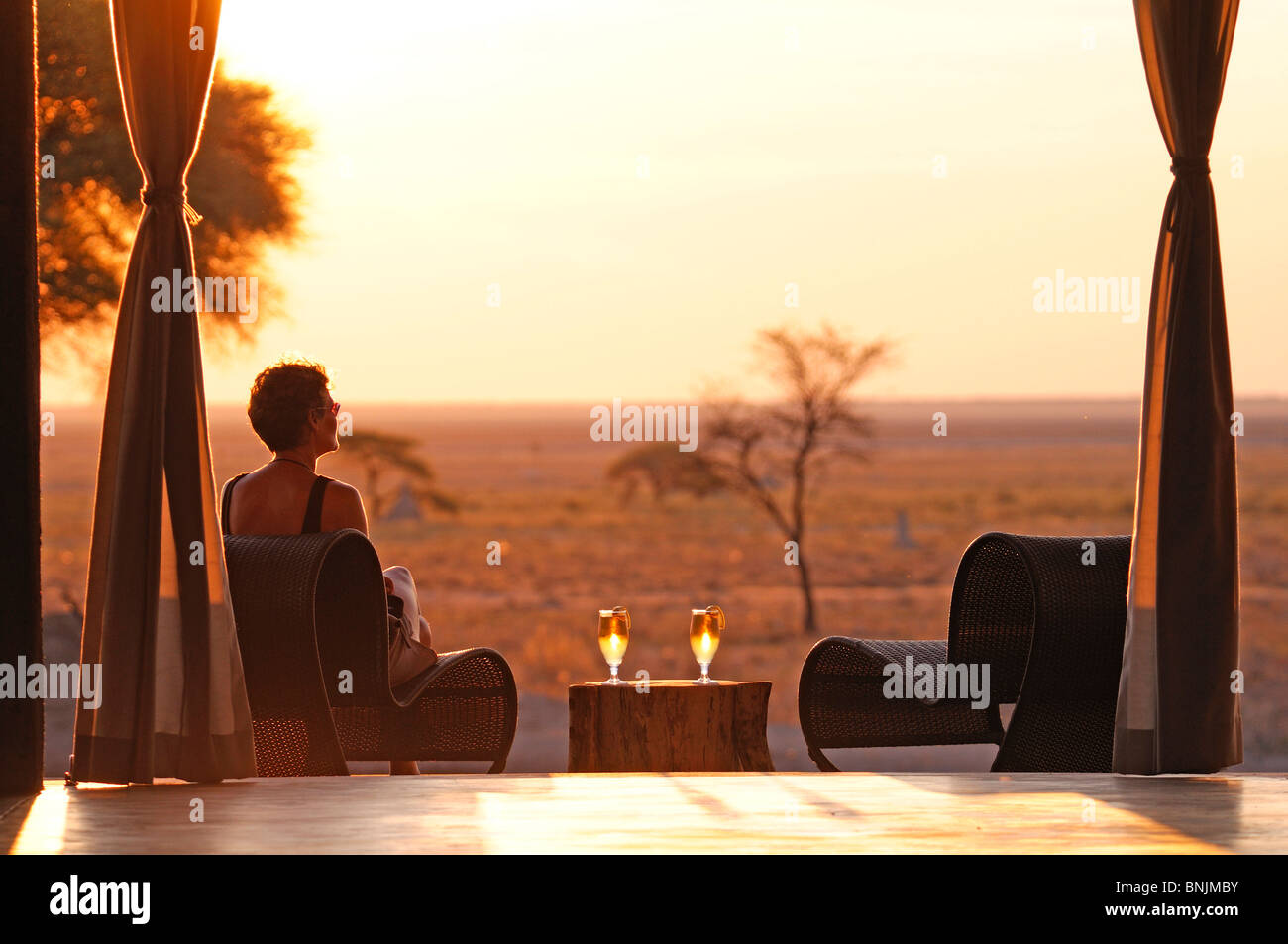 Sundowner Sonnenuntergang Drink serviert Deck Frau The Fort Fisher Pan Onguma Safari Camp Etosha Nationalpark Kunene-Region Namibias Stockfoto