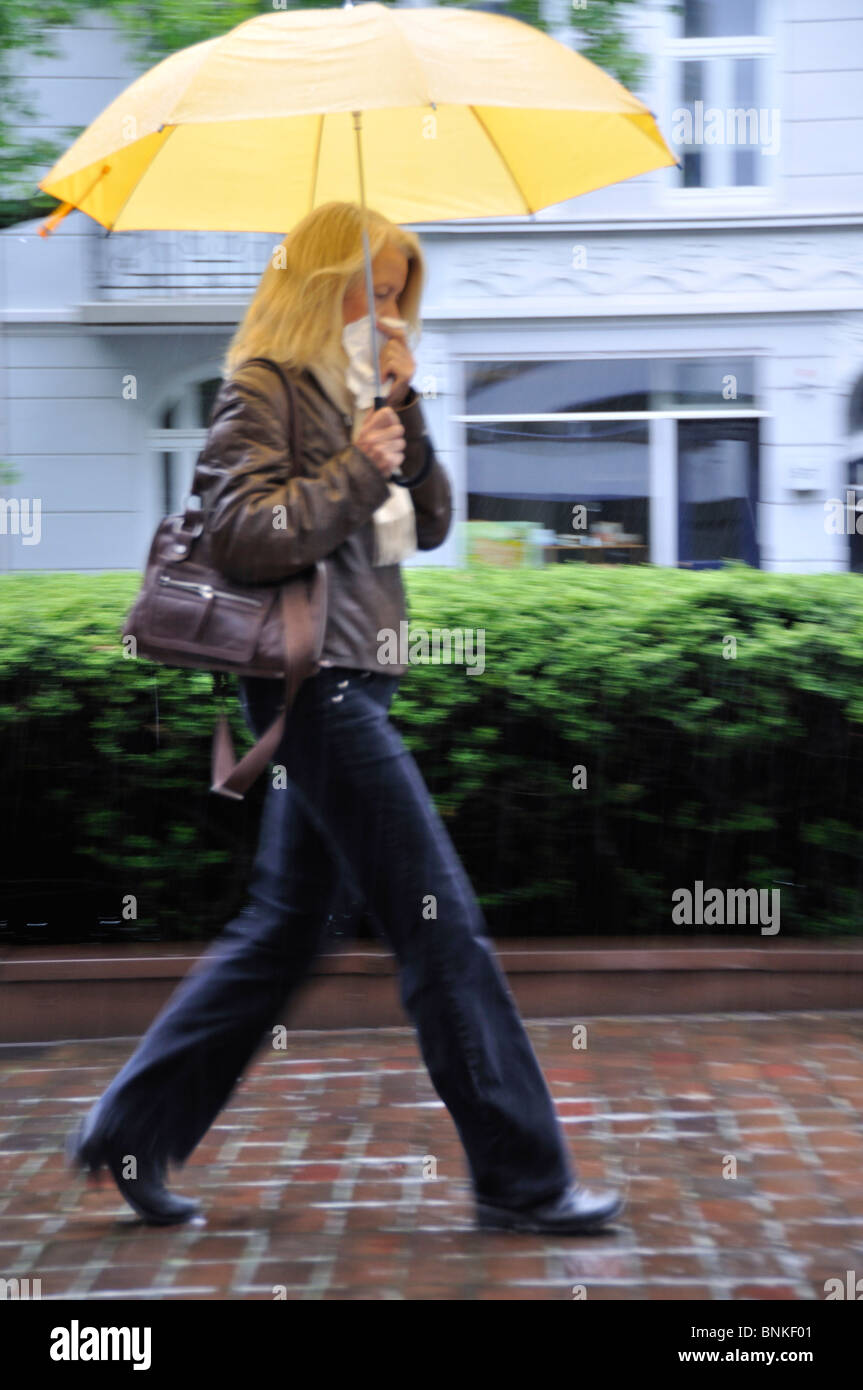 Person Frau Frau Blond bewegen gehen laufen zu Fuß auf dem Weg schnell nassen Regenschirm Regen Wetter Gewitter Wind ungestümer unbequem Stockfoto
