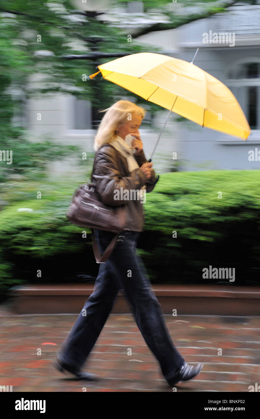 Person Frau Blond bewegen gehen laufen zu Fuß auf dem Weg schnell nassen Regenschirm Regen Wetter Gewitter Wind ungestümer unangenehm kalt Stockfoto