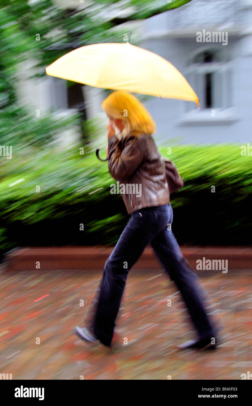 Person Frau Blond bewegen gehen laufen zu Fuß auf dem Weg schnell nassen Regenschirm Regen Wetter Gewitter Wind ungestümer unangenehm kalt Stockfoto