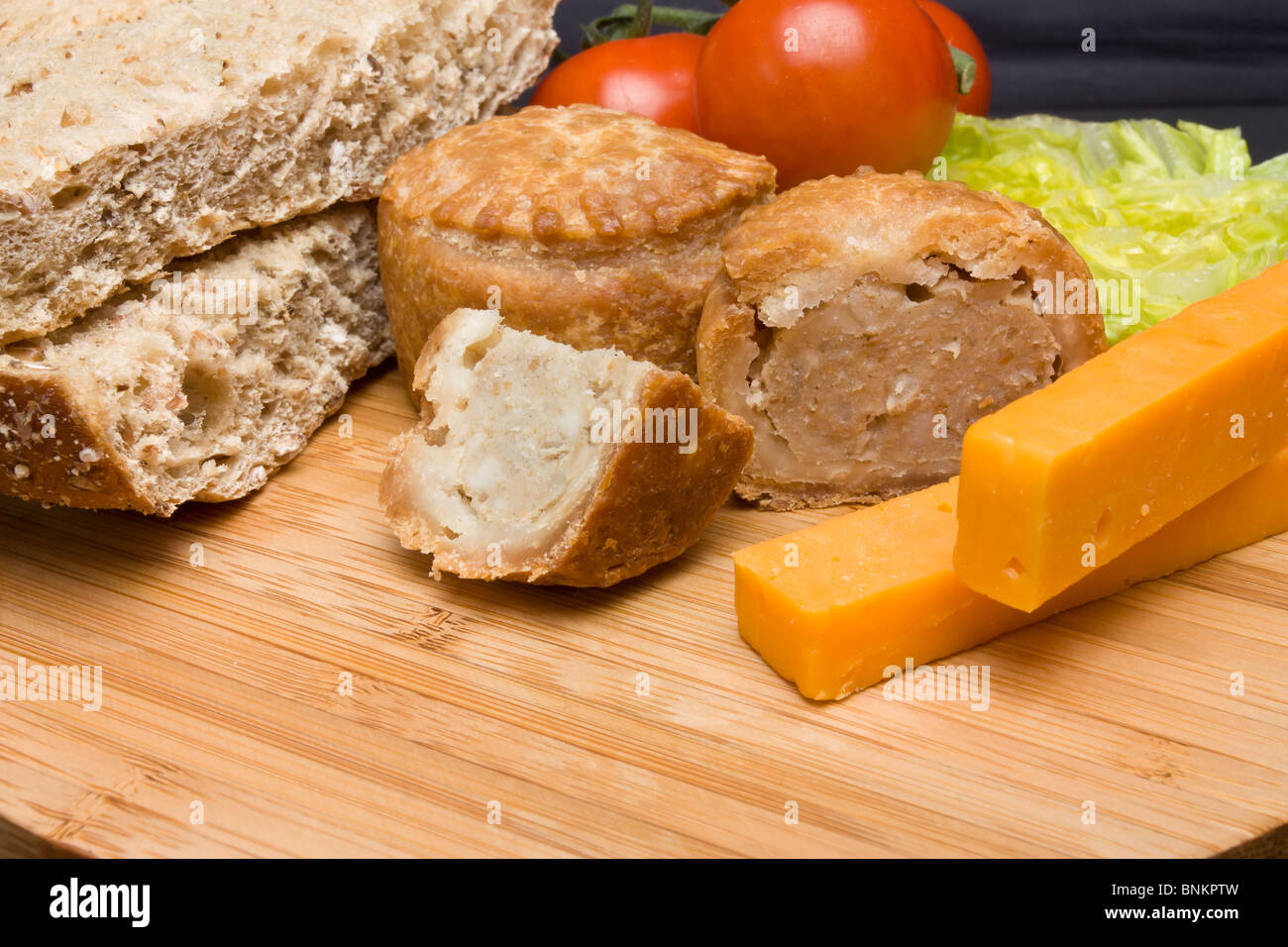 Traditionelle englische Ploughmans Lunch von Käse, Brot, Tomaten, Salat und Pork Pie auf hölzernen Platte. Stockfoto