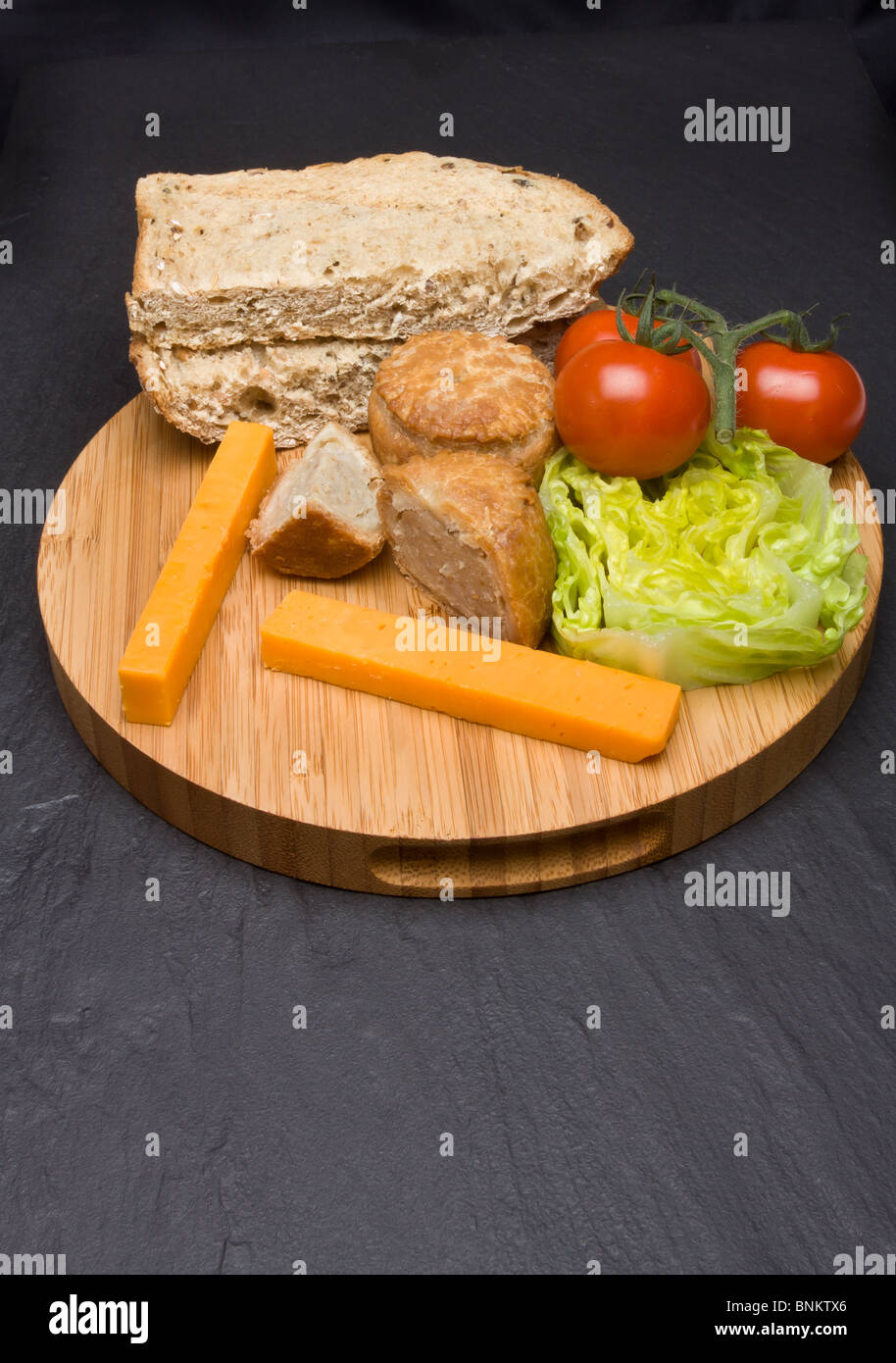 Traditionelle englische Ploughmans Lunch von Käse, Brot, Tomaten, Salat und Pork Pie auf hölzernen Platte. Stockfoto