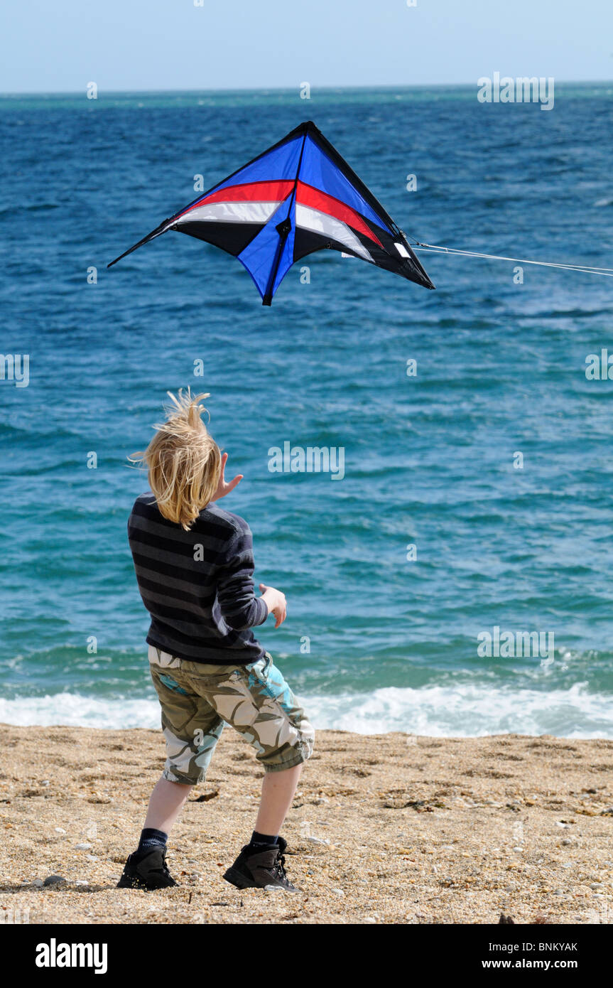 Junge lehnt sich zurück und beobachtete einen Drachen fliegen gerade über seinem Kopf an einem sonnigen Strand, nachdem er nur loslassen ist Stockfoto