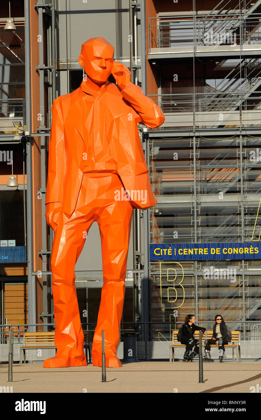 Ein Mann mit seinem Handy in der Nähe einer riesigen Statue zeigt einen Mann mit einem Mobiltelefon in der Cité Internationale in Lyon, Frankreich. Stockfoto