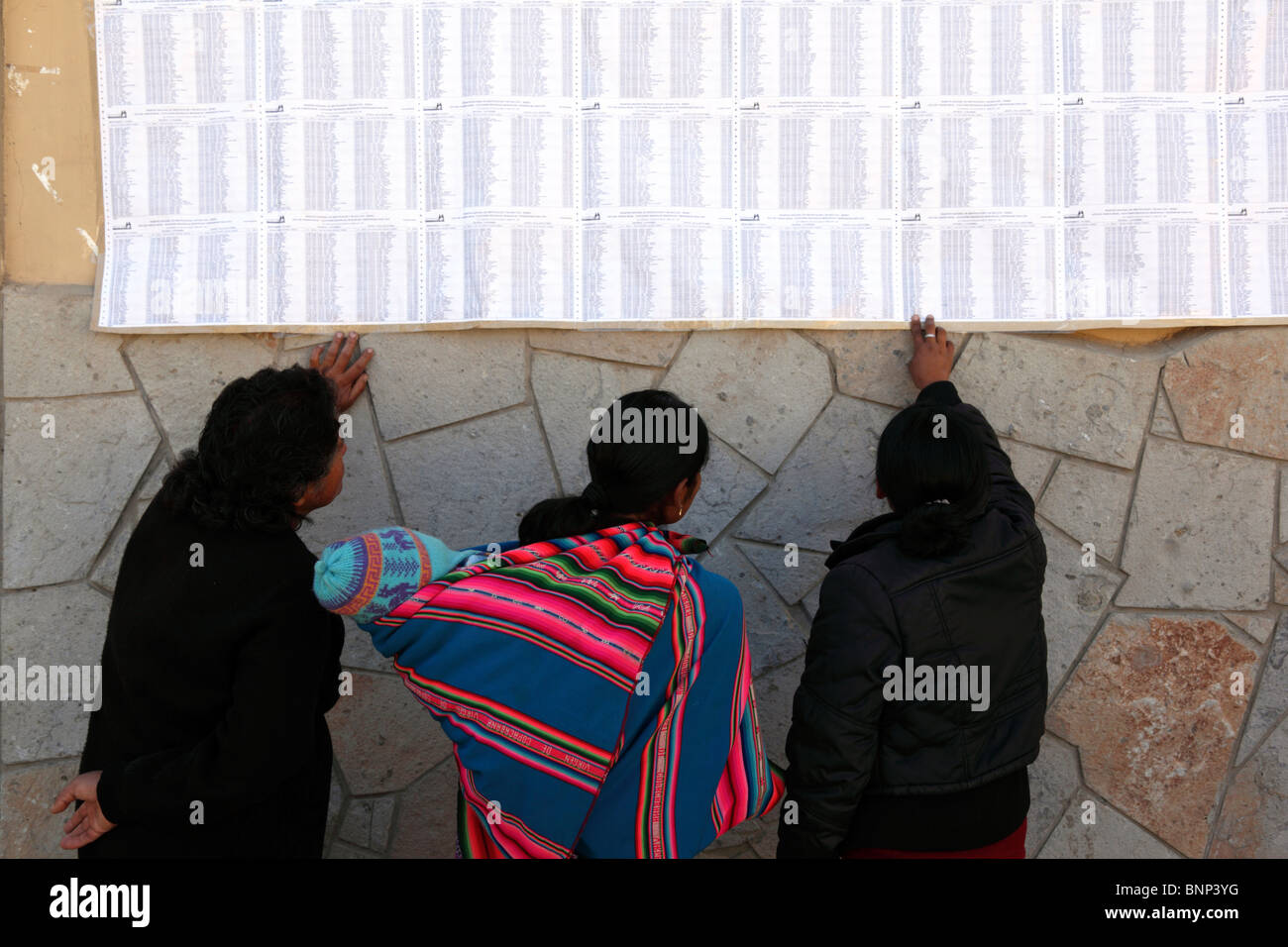 Die Leute suchen nach ihren Namen auf der Wahlliste an der Wand vor dem Rathaus im Dorf Ollantaytambo, Heiliges Tal, Region Cusco, Peru Stockfoto