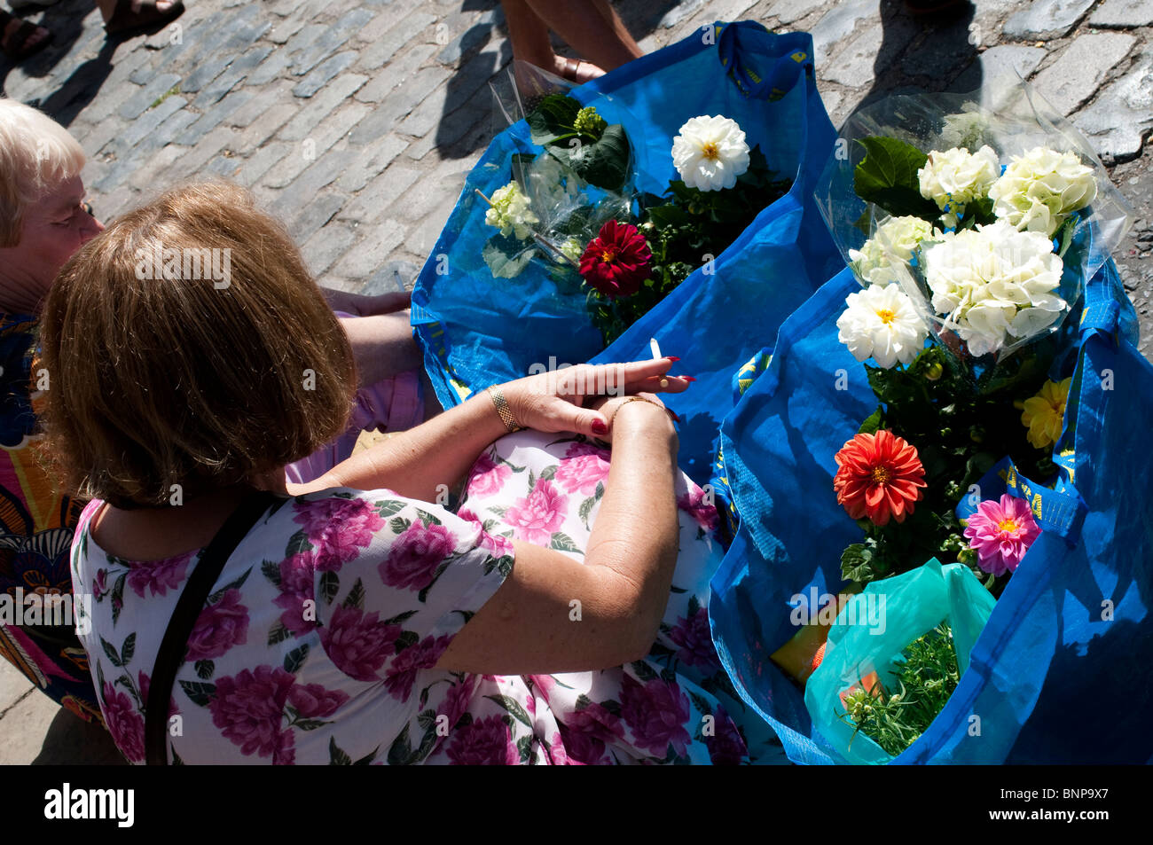 Menschen sitzen auf den Bordstein des Belags und entspannen in der Nähe von Columbia Road Market, London, E2, England, UK Stockfoto