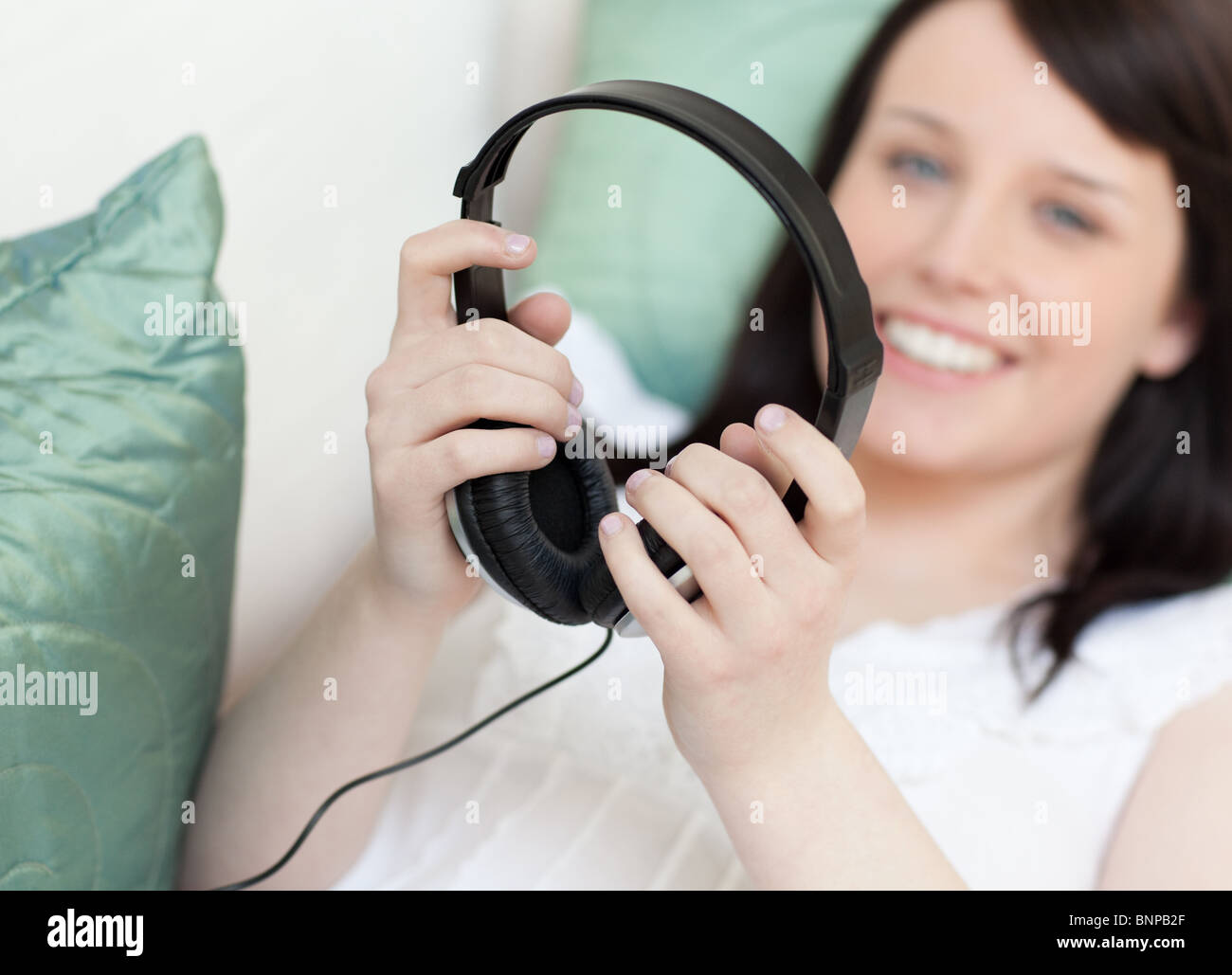 Lächelnde junge Frau setzen Kopfhörer auf einem Sofa liegend Stockfoto