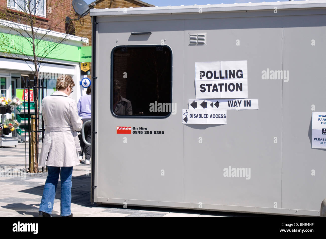 Eine Frau mit einer Polling-Karte in der Hand nähert sich einem temporären Wahllokal am Wahltag in England Stockfoto
