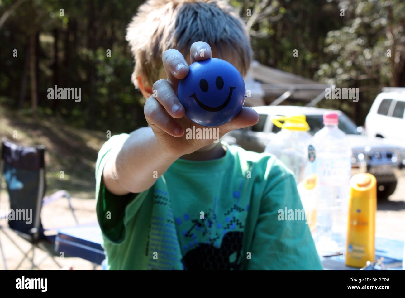 Kleiner Junge bedeckte sein Gesicht mit einer blauen Smiley-Kugel Stockfoto