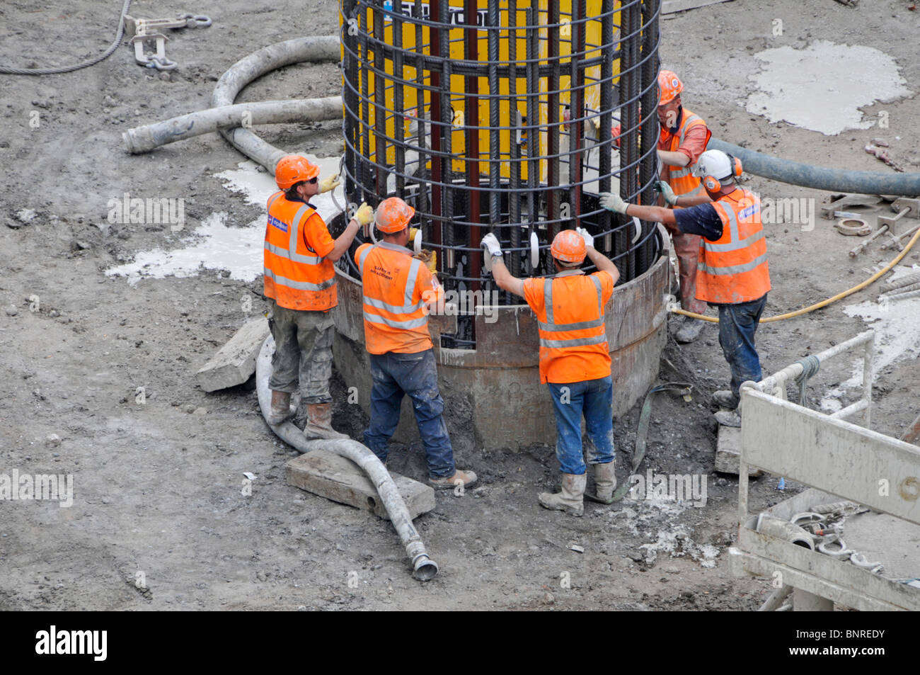 Baustellenarbeiter arbeiten im Team zusammen Stahlkäfig von Kran in Pfahl Gehäuse Fundamente Canary gehalten Wharf Crossrail Großbritannien Stockfoto